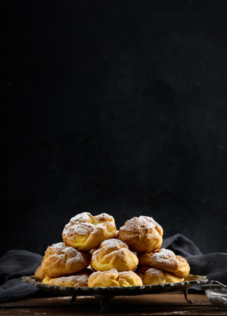 Baked eclairs with custard cream on a metal round plate sprinkled with powdered sugar