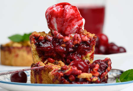 Cherry crumble pie decorated with a scoop of ice cream and drizzled with cherry sauce on a plate