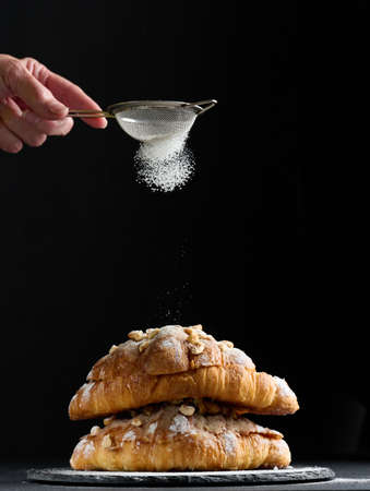 Baked croissant on a board and sprinkled with powdered sugar, black table. Appetizing pastries for...