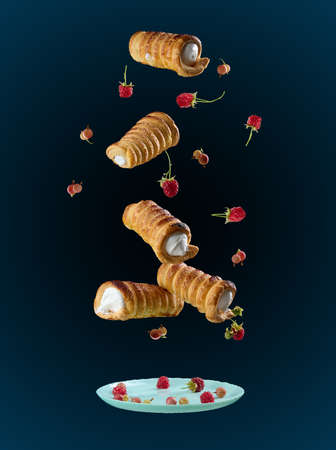 Baked crispy tubes with whipped protein cream levitate on a black background, powdered sugar pours...