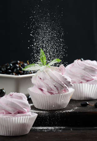 Portioned fruit marshmallows in a paper cup on a black wooden board, delicious dessert