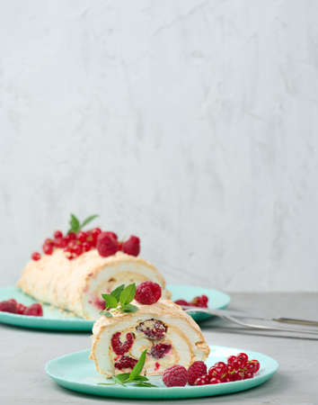 Baked meringue roll with red berries on a round plate, white backgroundの写真素材