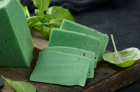 A piece of green cheese with basil on a brown wooden board, black background