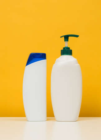 Plastic bottles with a pump for shampoo, shower gel on a white table, yellow backgroundの写真素材