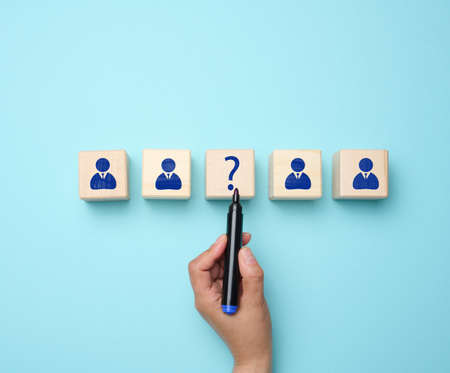 Wooden figures of men and a woman's hand drew a question mark with a marker on a blue background....