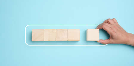 A woman's hand holds wooden cubes on a blue background. The concept of loading the process, the beginning of new achievementsの写真素材
