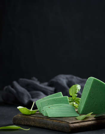 A piece of green cheese with basil on a brown wooden board, black backgroundの写真素材