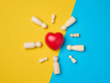 Red heart and wooden figurines of men on a yellow-blue background, top viewの写真素材