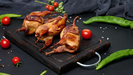Frying carcasses of quails lie on a wooden board with vegetables, a black tableの写真素材