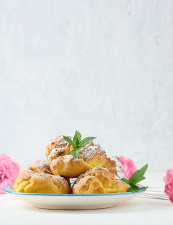 Baked eclairs with custard cream on a round plate sprinkled with powdered sugarの写真素材