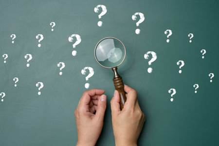 Female hand holds a plastic magnifying glass and question marks on a green background. The concept of finding an answer to questions, truth and uncertainty.の写真素材