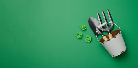 Miniature garden tools in a metal bucket on a green background, top viewの写真素材