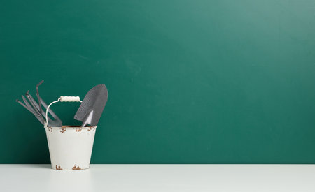 Miniature garden tools in a metal bucket on a green background, copy spaceの写真素材