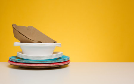 Stack of disposable paper plates on yellow background, copy space