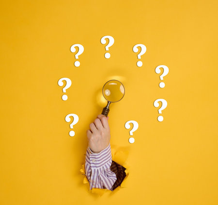 Female hand holds a magnifying glass on a yellow background, part of the body sticks out of a torn hole in a paper background. Business concept, finding information, answering questionsの写真素材