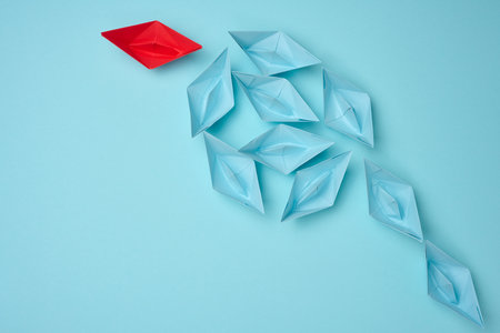 Group of blue paper boats heading in one direction and one red one heading in the opposite...