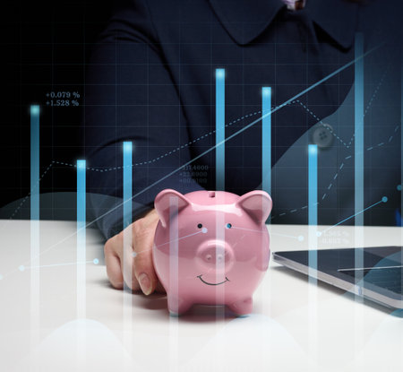 Woman in a suit sits at a table and works on a laptop, next to it is a ceramic piggy bank. Business indicators growth concept, enterprise analysis. Paying taxesの写真素材