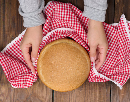 Round baked bread on a wooden board, brown table. View from aboveの写真素材