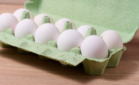 Fresh whole white eggs in green paper packaging on a wooden table