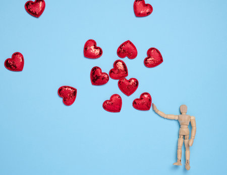Wooden mannequin toy and red hearts on a blue background, concept of loveの写真素材