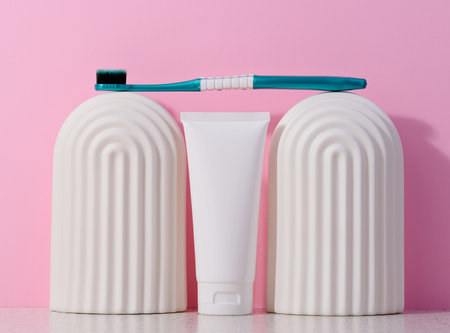White plastic toothpaste tube and toothbrush on a pink background.