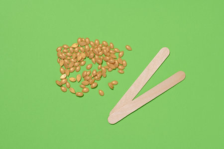 Wooden sticks for applying wax and yellow wax granules for cosmetic procedures on a green...