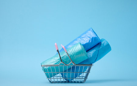 Rolls of plastic bags in a miniature shopping basket on a blue backgroundの写真素材