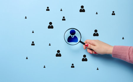 A woman's hand holds a magnifying glass and focuses on a leadership badge, the concept of human resource management, personnel recruitment, target audienceの写真素材