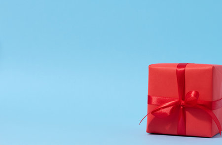 A square red gift box with a red ribbon on a blue background, congratulatory backdrop, surprise. copy spaceの写真素材