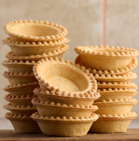 Stack of empty baked round canape baskets on a wooden board, round empty tartletsの写真素材