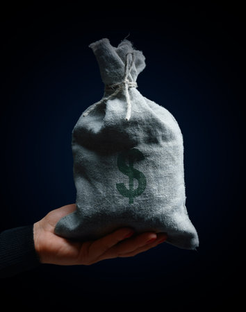 A female hand holding a full burlap sack with a dollar sign, concept of wealth, profitable businessの写真素材