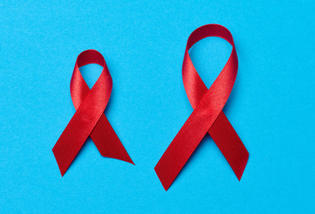 A silk red ribbon in the form of a bow on a blue background, a symbol of the fight against AIDS and a sign of solidarity and supportの写真素材