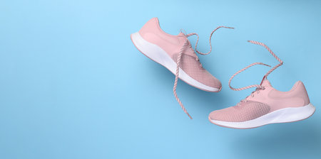 Pink women's sports sneakers with laces levitate on a blue background. copy spaceの写真素材