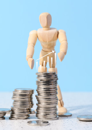 Wooden mannequin and a stack of coins on a blue background. Business indicators growth concept, income growthの写真素材