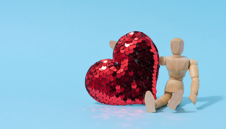 Wooden mannequin and red heart made of sequins on a blue backgroundの写真素材