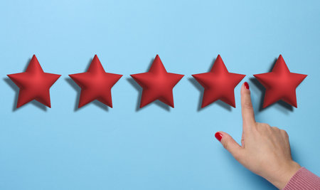 Five red stars and a hand on a blue background. Evaluation of the quality of services and goods, high ratingの写真素材
