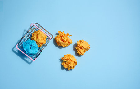 Crumpled balls of paper in a miniature shopping cart on a blue background. New ideas and innovationsの写真素材