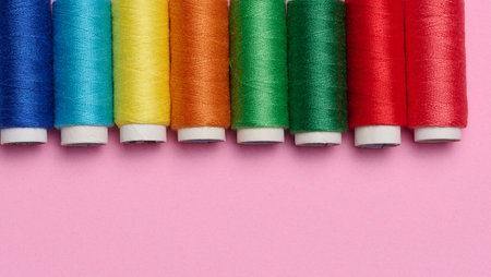 Multicolored spools of sewing threads on a pink background, top viewの写真素材