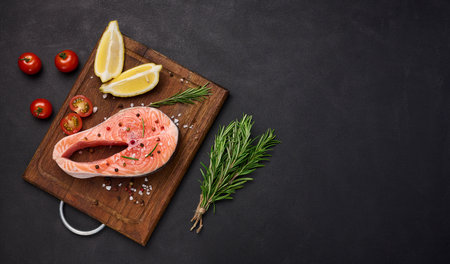 Raw salmon steak on a wooden cutting board, lemon slices, spices. Top view on black table. copy spaceの写真素材