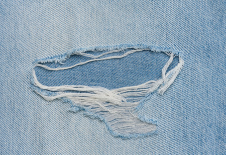 Fragment of blue jeans fabric with a hole, full frame, close up