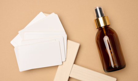 Glass brown bottle with cosmetic spray and paper business cards on brown background, top viewの写真素材