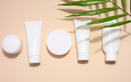 White plastic tubes, jars, and gypsophila branches on a beige background, containers for cosmetic creams and gels, advertising and brand promotion, top viewの写真素材