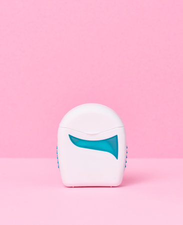 White plastic packaging with dental floss on a pink background, close up