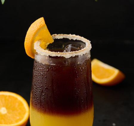 Iced coffee with orange juice in a transparent glass, refreshing bumble coffee on the table, black backgroundの写真素材