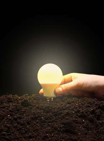 A female hand holds an electric glowing light bulb above the ground, symbolizing the concept of...