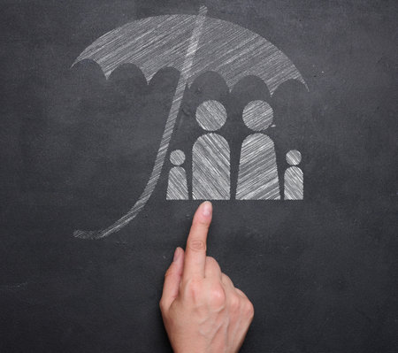 A family drawn in white chalk under an umbrella on a black chalkboard and a female hand, symbolizing the concept of security and insurance.の写真素材