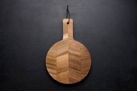 Round wooden kitchen cutting board with handle on a black background, top view
