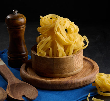 Raw long noodles made from white wheat flour in a wooden bowl on a black tableの写真素材