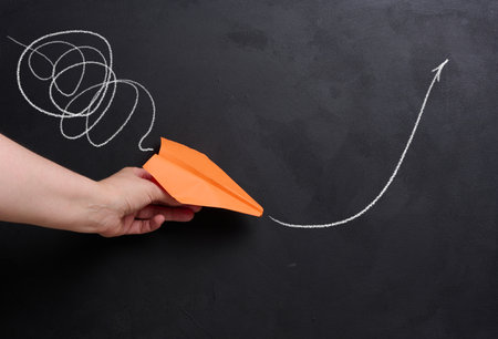 A hand holds a paper airplane with a drawn flight trajectory on the board, representing the concept...