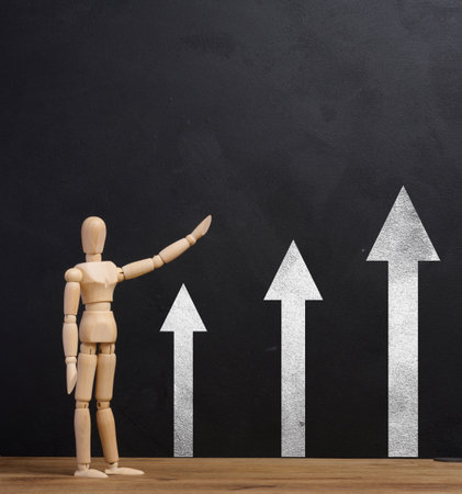 Wooden mannequin points at black chalk board with arrows, growth indicators